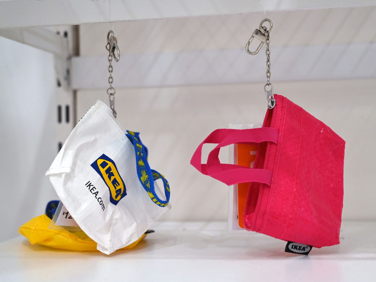 Keychains designed as bags, one yellow, one bright pink, and one white with the text IKEA in blue and yellow.
