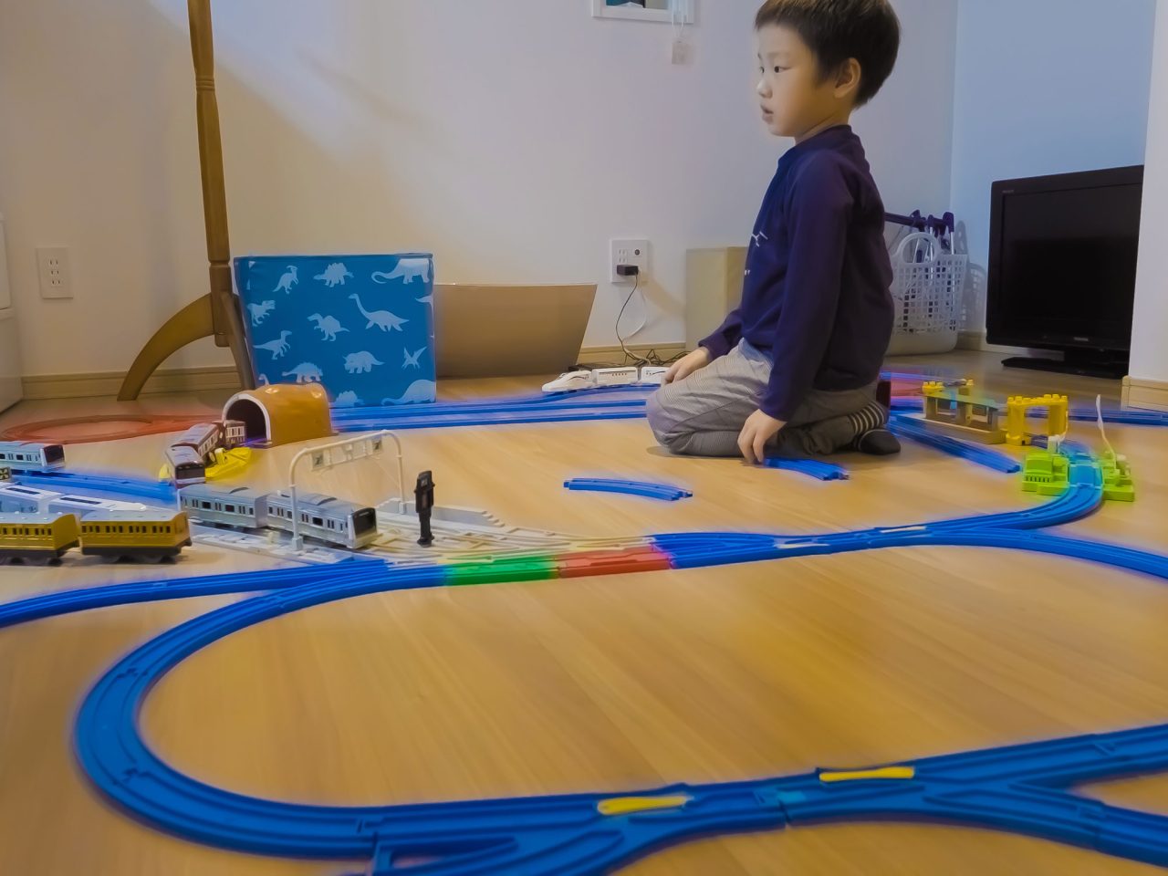 Small child sitting on parquet floor playing with a large train track.