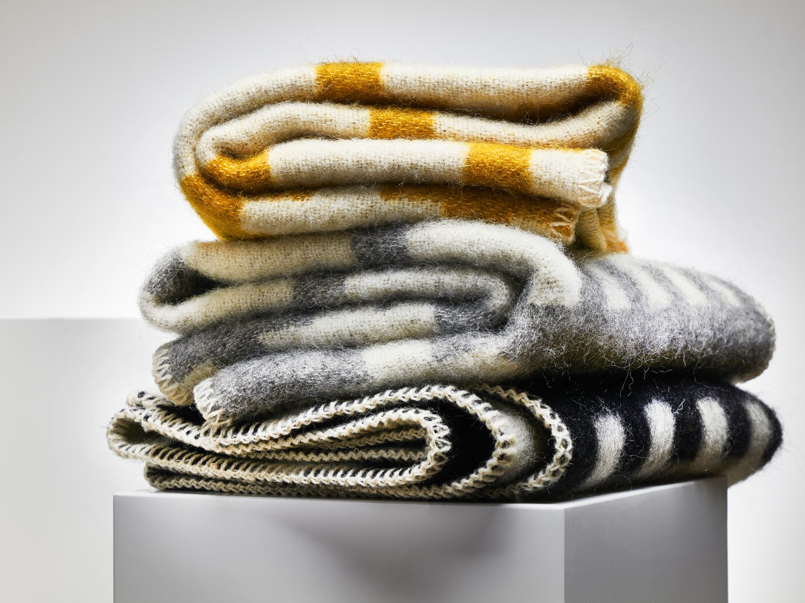 Stapel gefalteter Wolldecken in Weiß und Grau, Schwarz und Gelb.
