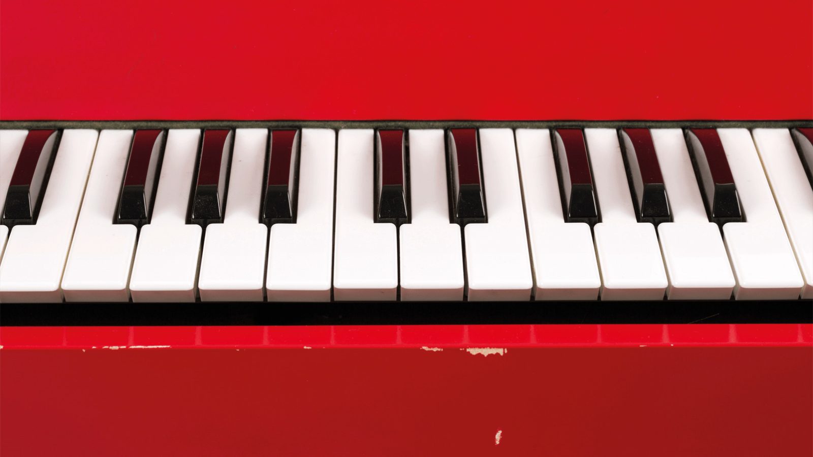 Close-up of a red, worn electric organ with black and white keyboard.