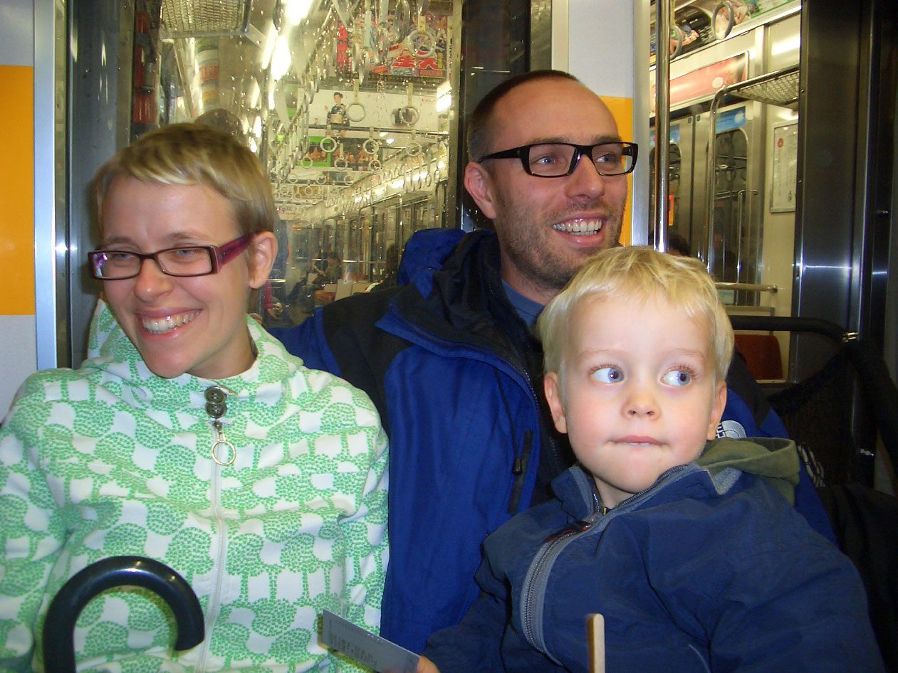 Leende blond kvinna och man, båda i svartbågade glasögon, med en liten blond pojke i blå fleecetröja.
