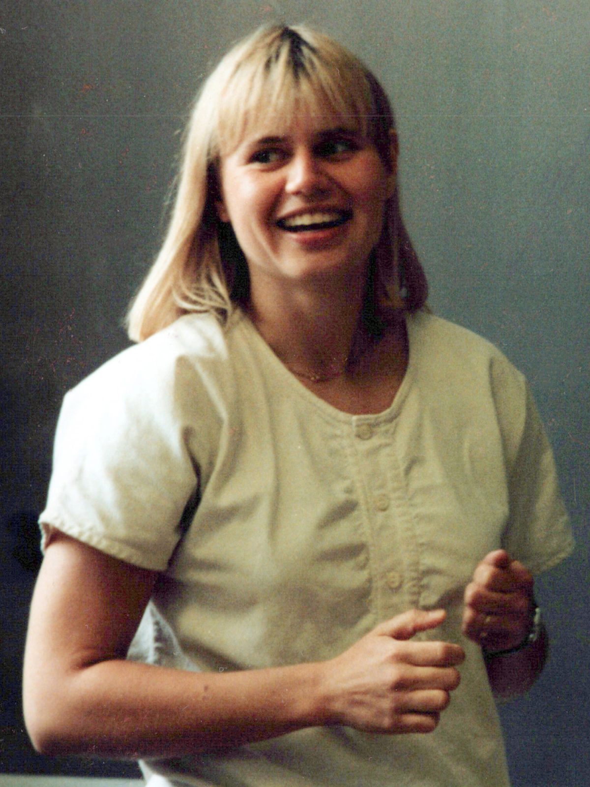 Młoda blondynka z szerokim uśmiechem, ubrana w bluzkę w stylu lat 80. XX w.