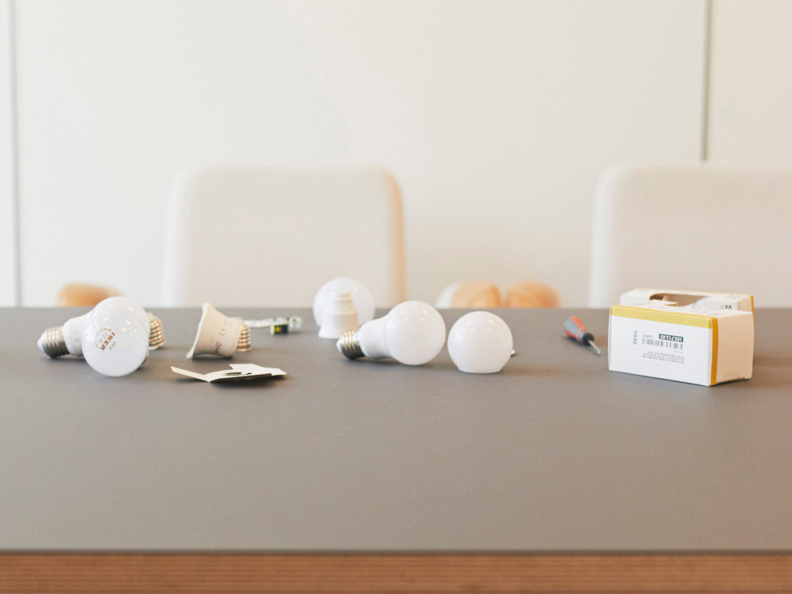 Gros plan sur tournevis et ampoules LED, certaines démontées, disposés sur un plateau de table gris.