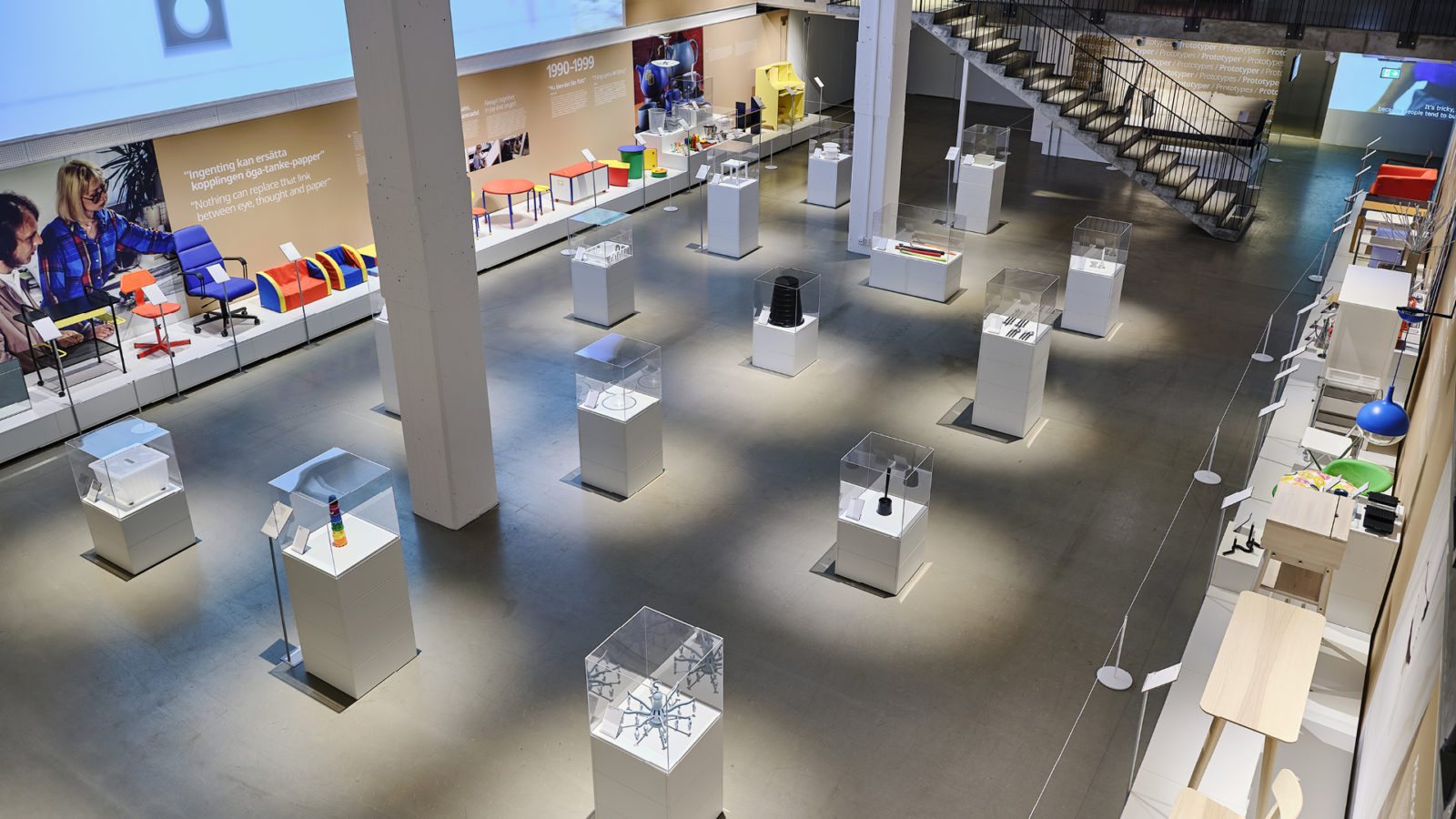 Exhibition hall with objects displayed in glass cabinets, and on a low podium against a beige wall with white information text.