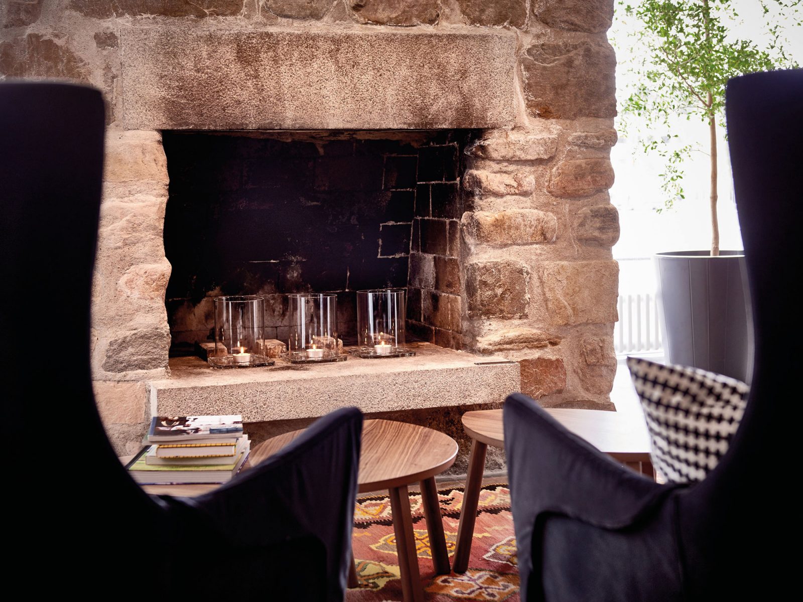 Two armchairs in front of low wooden tables and brick fireplace.