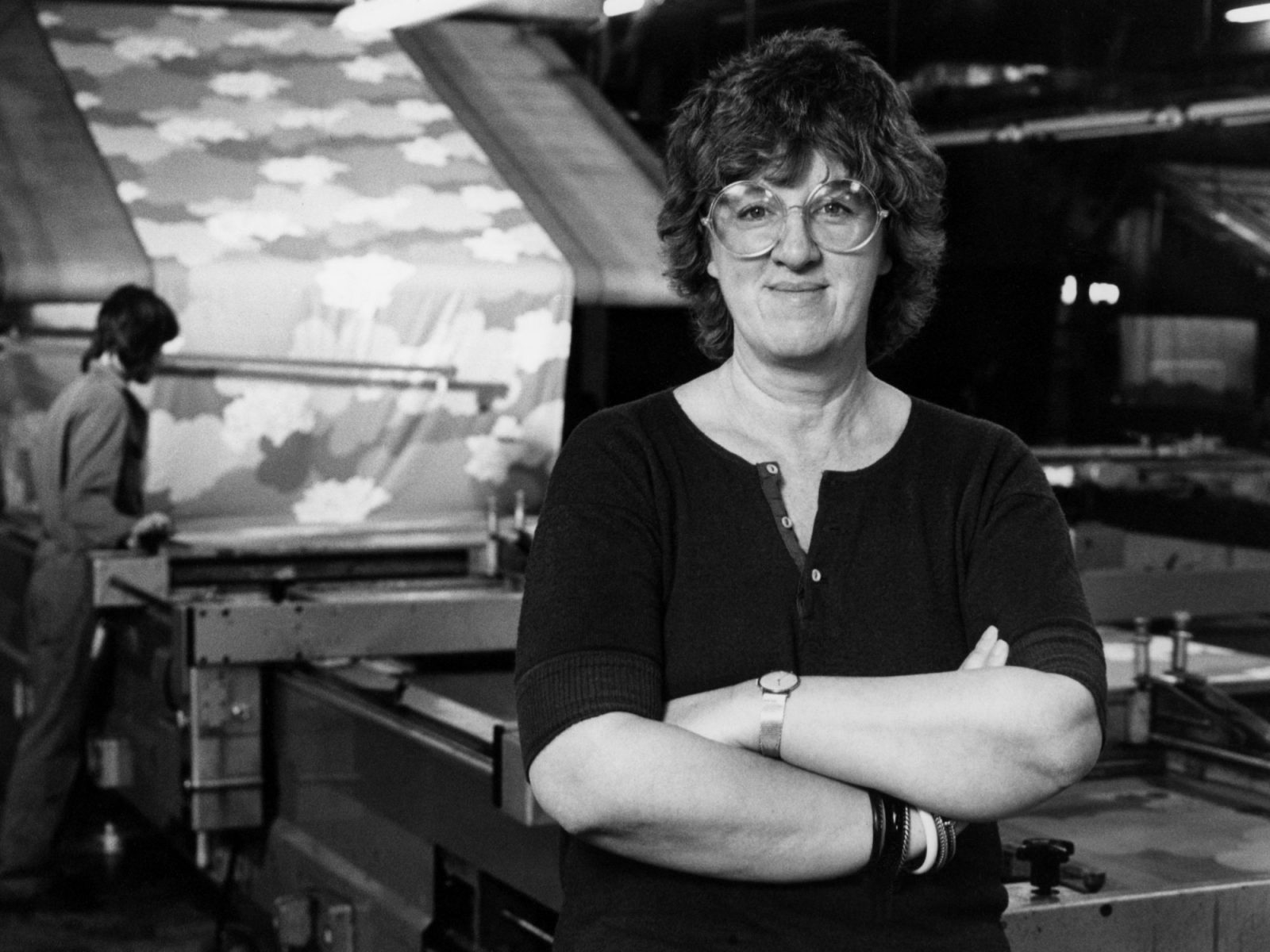 Woman with dark hair and big glasses in 1970s style, Inez Svensson, standing in front of a textile printing machine.