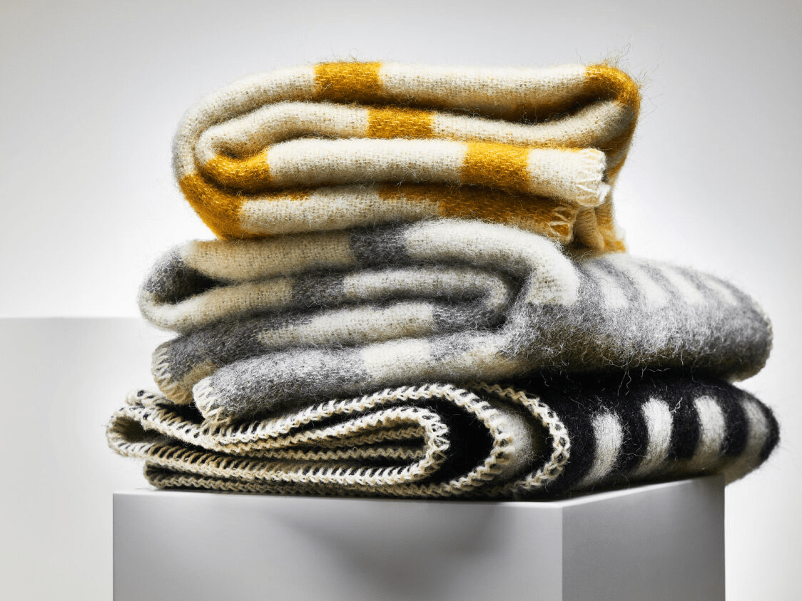 Stack of folded wool blankets in white and grey, black, or yellow.