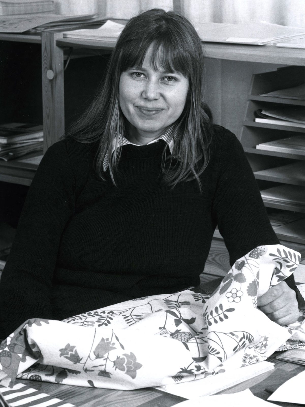 Smiling young woman with long hair holding a floral-patterned fabric.