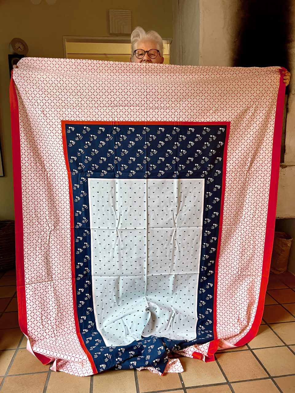 White-haired woman, Vivianne Sjölin holding a patchwork quilt made of various blue, red, and white patterned fabrics.
