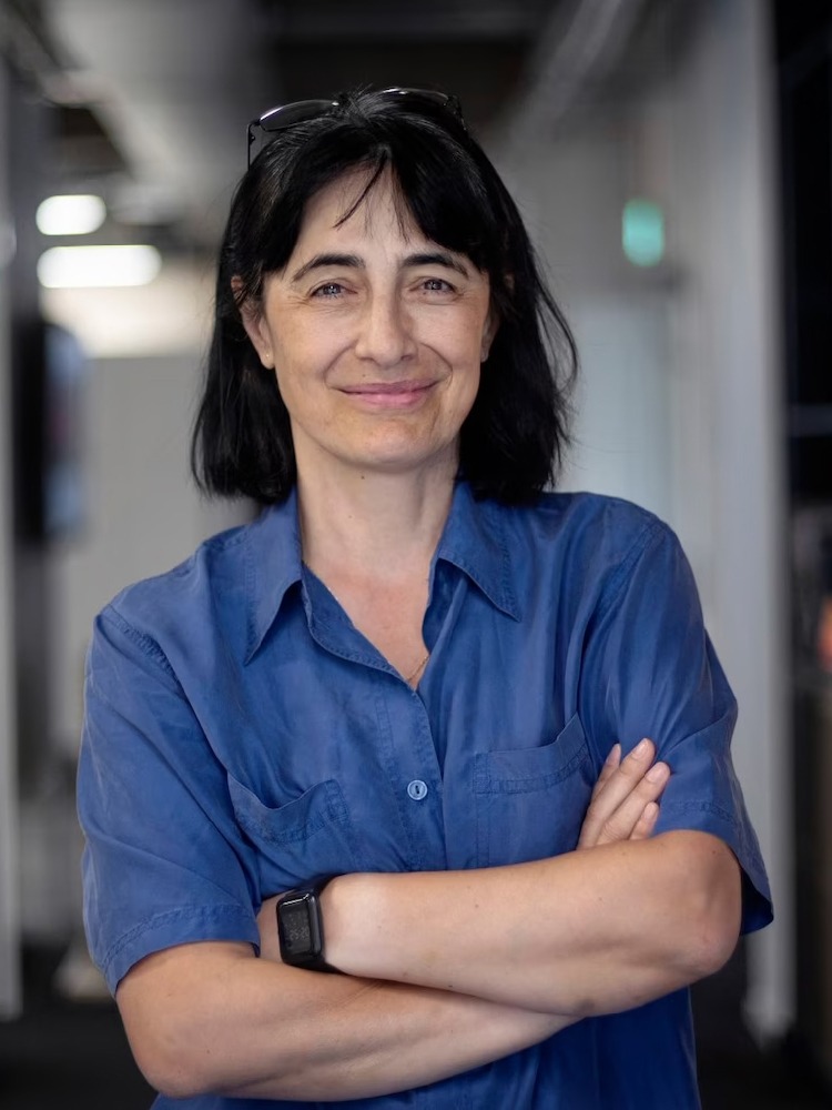 Dark-haired smiling woman in blue shirt, arms crossed, Carmen Stoicescu.