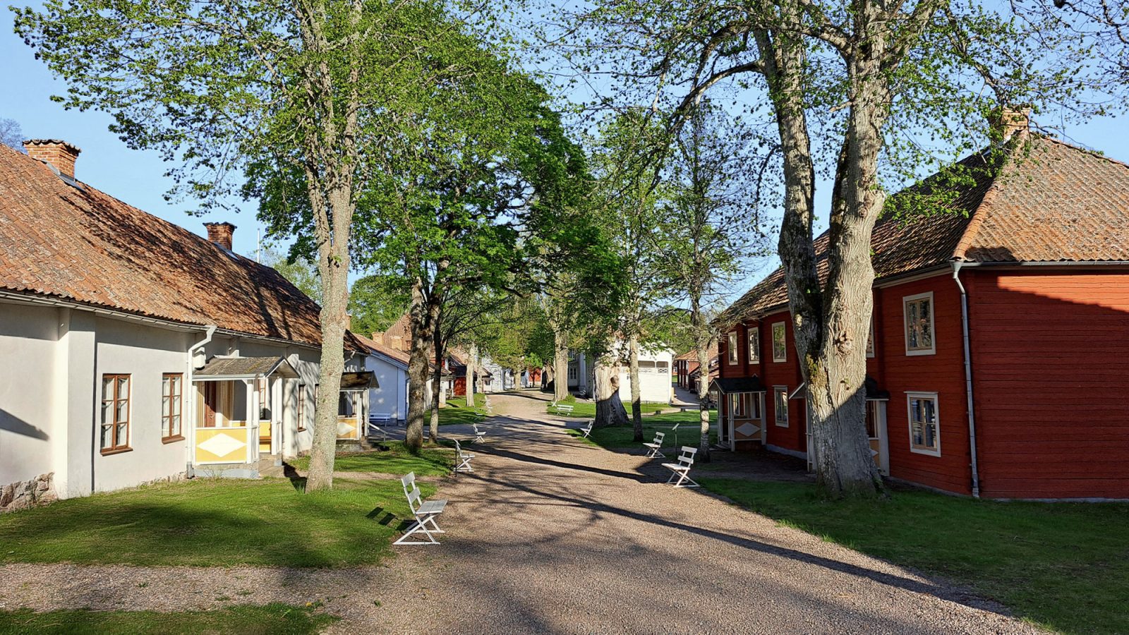 Grusväg kantad av äldre byggnader och lummiga träd, Medevi Brunn.