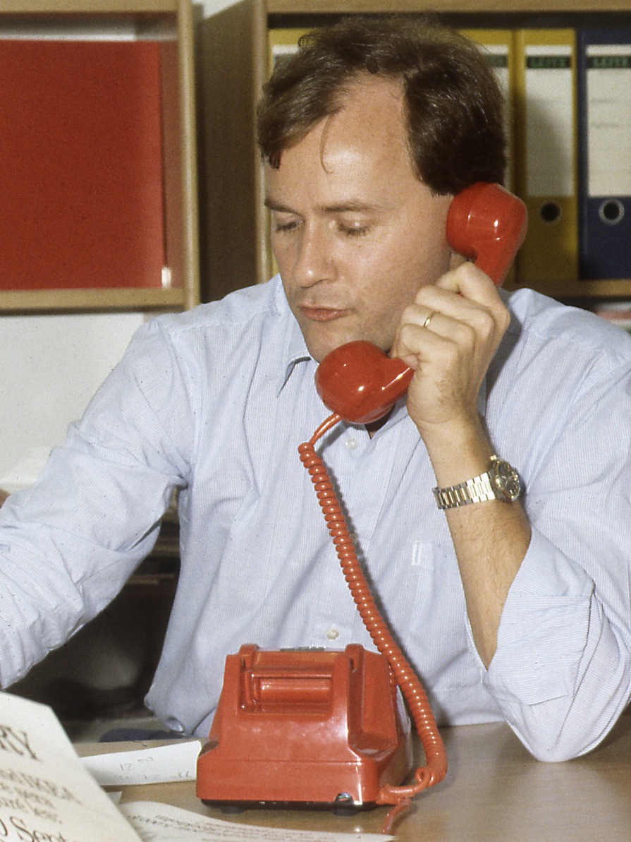 Man i ljusblå skjorta, Janne Kjellman, pratar i en röd telefon.