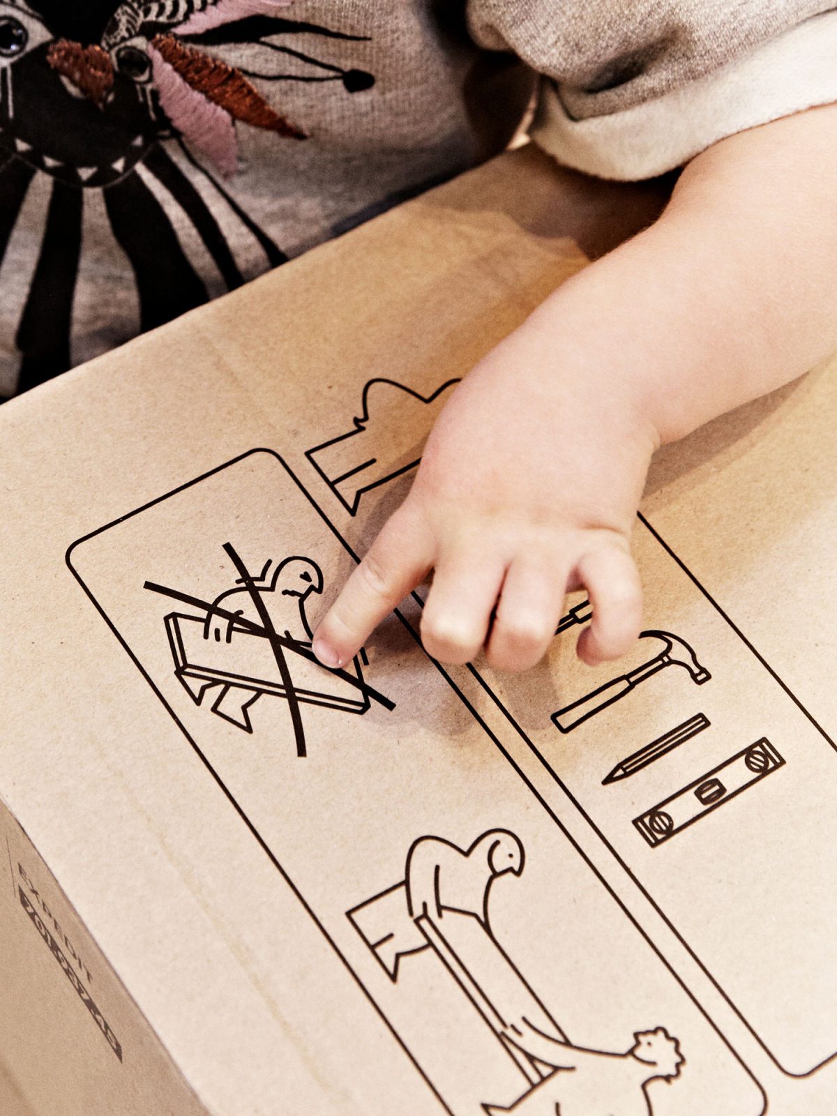 Liten barnhand pekar på en teckning på ett platt paket från IKEA, som visar hur förpackningen ska bäras.
