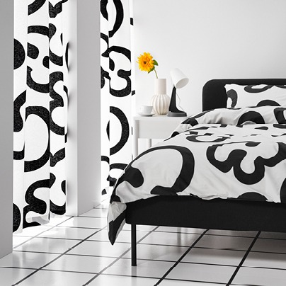 Bedroom with bold patterned black and white curtains and bedset, a yellow flower in a white vase.