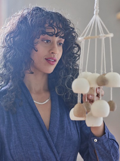 Dark-haired woman in blue shirt, Akanksha Deo, studies a hanging mobile with white and beige balls.
