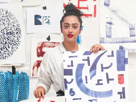 Dark-haired woman in white shirt, Akanksha Deo, surrounded by colourful sketches.