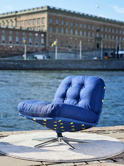 Blue swivel chair decorated with small yellow crowns in front of Stockholm Royal Palace.