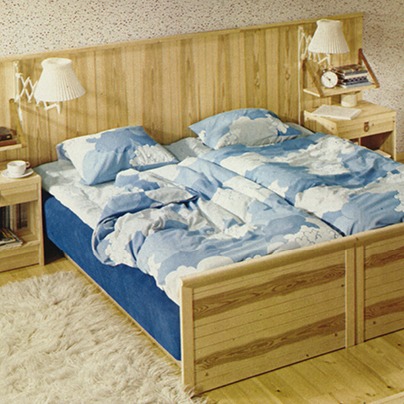 1970s style bedroom, pine bed made up with bedsheets with a cloud pattern.