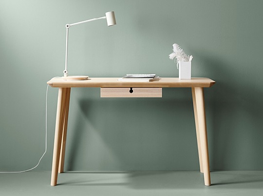 Simple blond wood desk placed against a green wall.