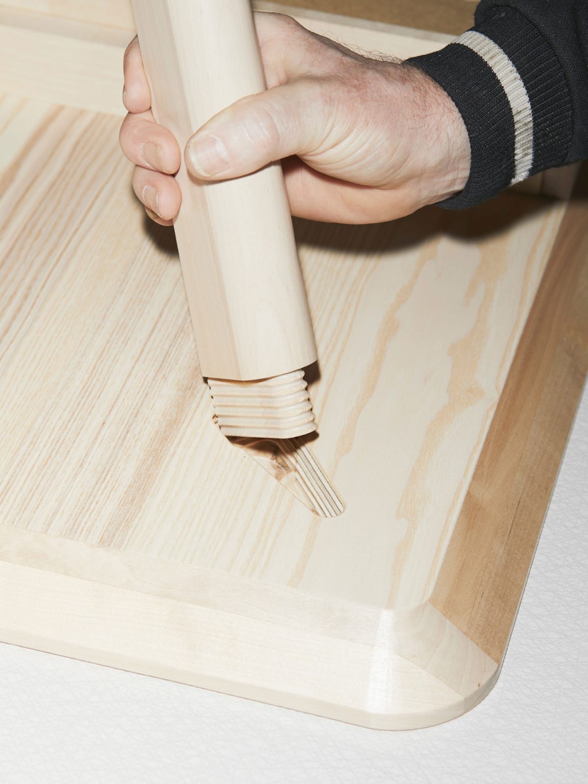 Close-up of a hand fastening a leg to a table with a wooden peg.