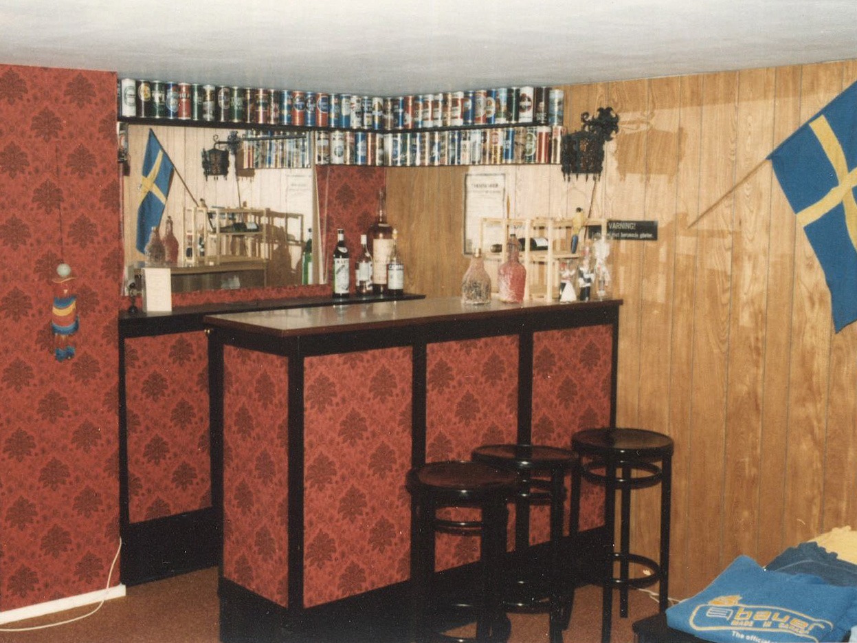 A homemade bar with bottles and glasses, and a Swedish flag hanging on the wall.