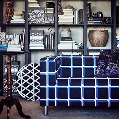 Sofa with a bold checked black, white and blue pattern stands in front of a bookcase.