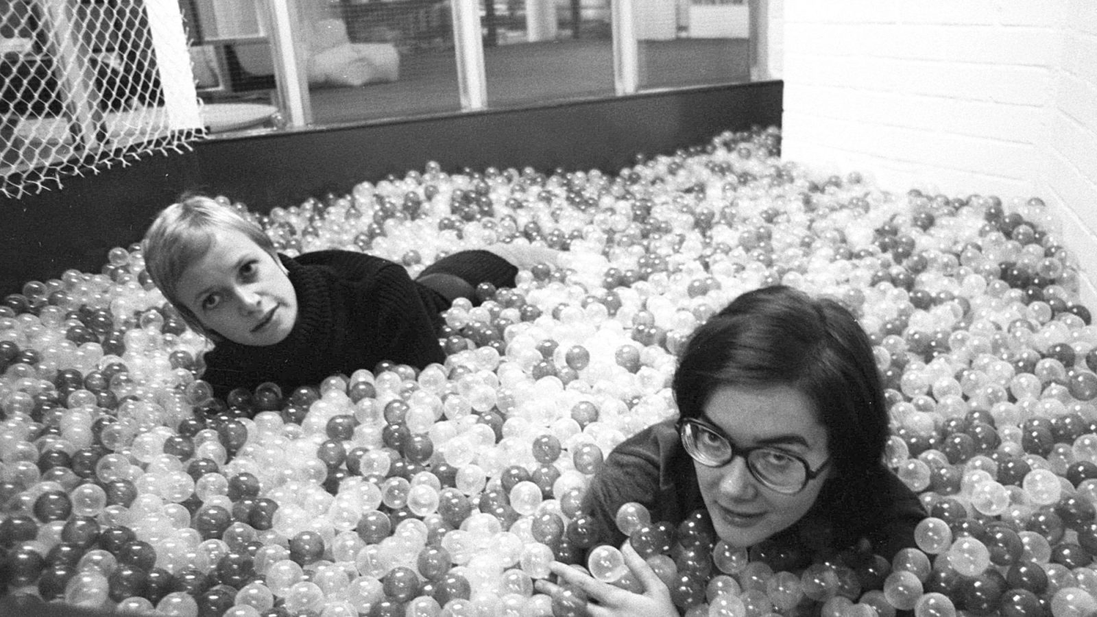 Two young women play in a large ball pit.