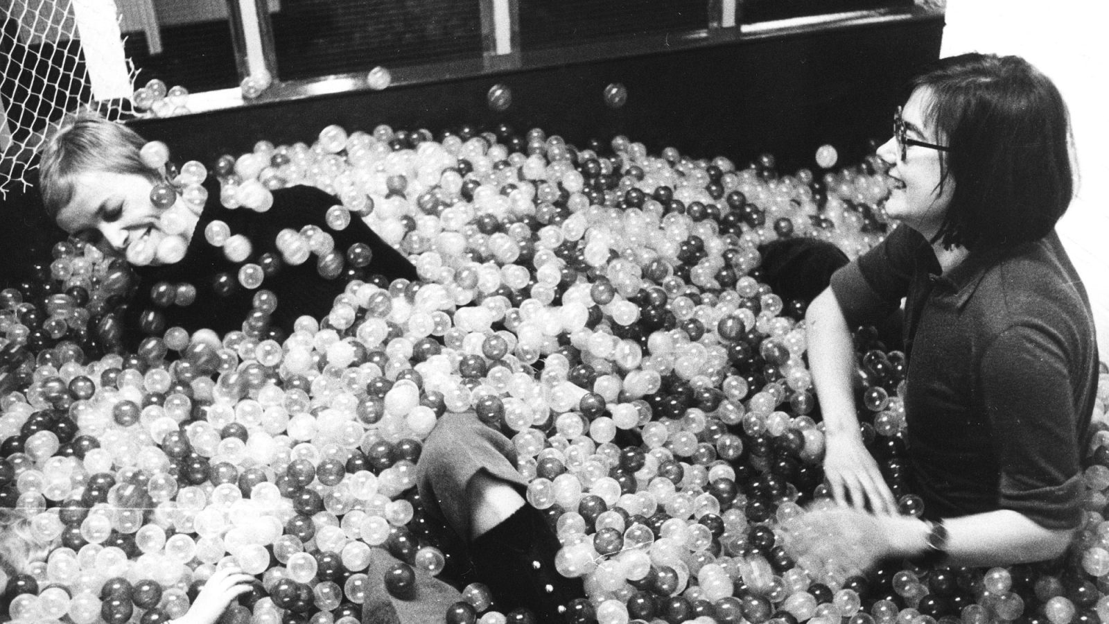 Two young women play in a large ball pit.