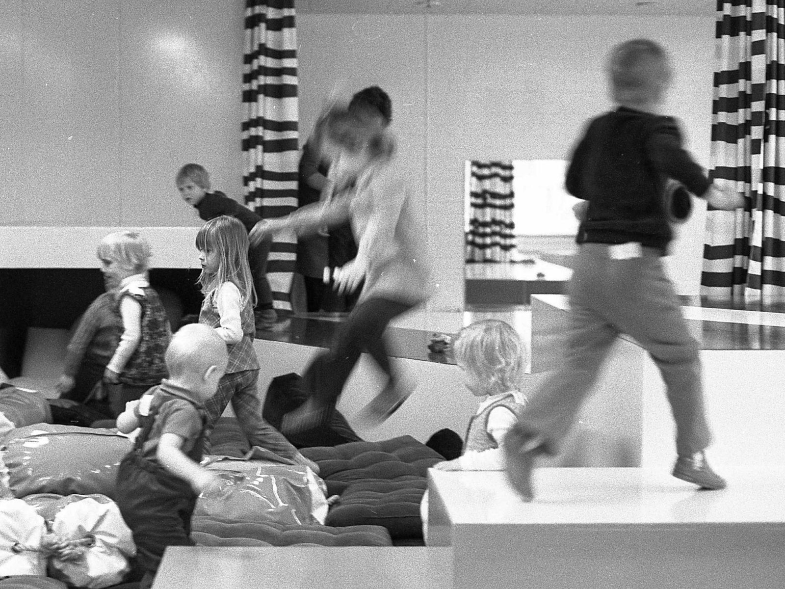 Children jump and play in a large playroom with soft cushions.