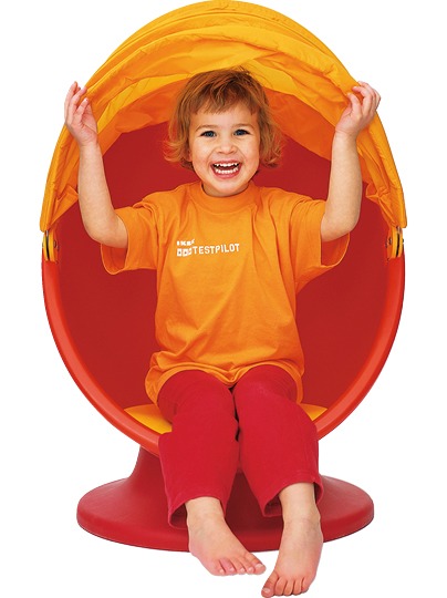 Smiling child sitting in red swivel chair with an orange hood, IKEA PS LÖMSK.