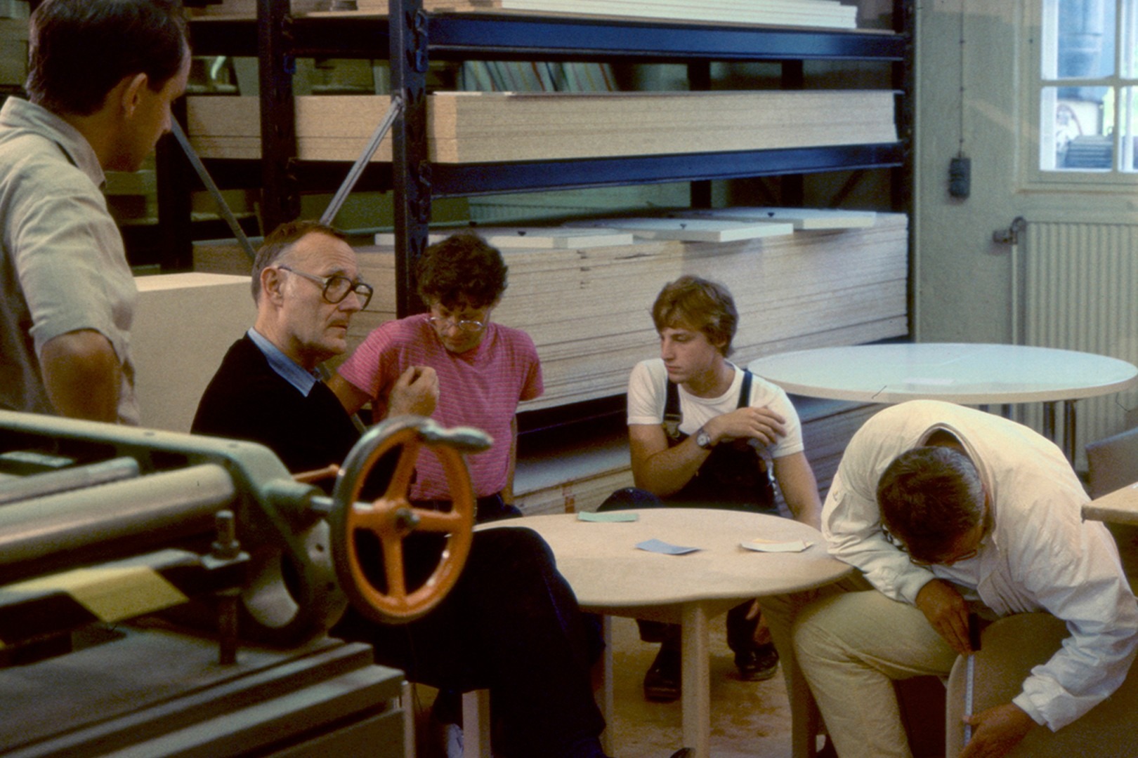Ingvar Kamprad sitting with co-workers in a factory, discussing around a table with wooden boards in the background