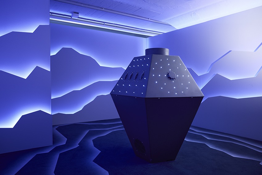Ein blau beleuchteter Raum mit Weltraumthema, mit einer interaktiven Einheit in der Mitte.