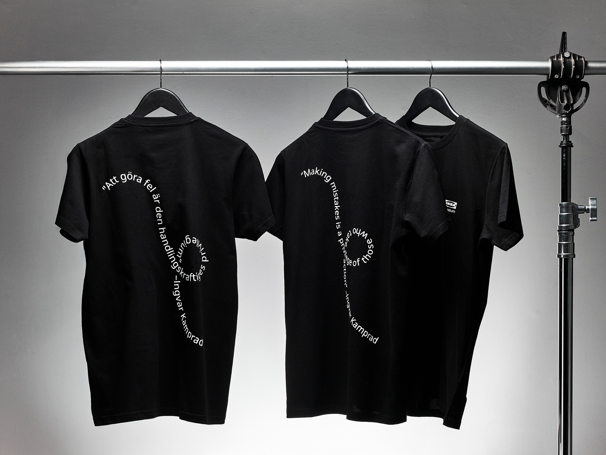 Drei schwarze T-Shirts mit weißem, wellenförmigem Text.